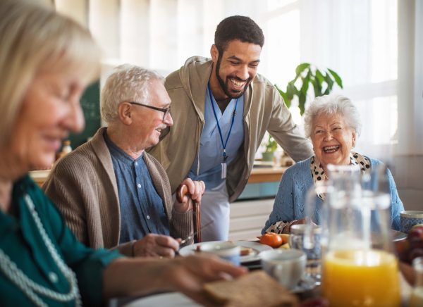 Pfleger lacht mit Rentnern beim Frühstück